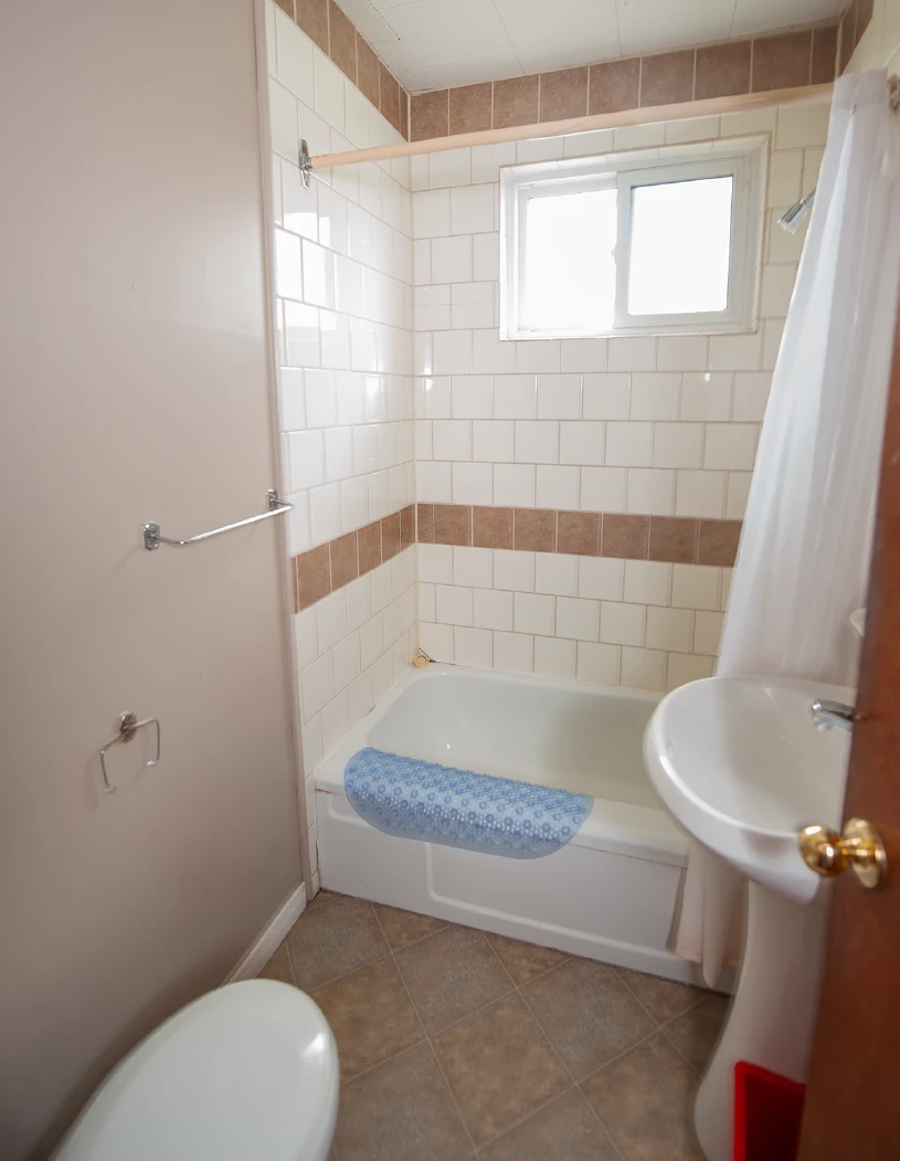 Pigeon Lake Resort Cottage five.&nbsp; Cottage bathroom with bathtub shower, tiled walls, pedestal sink, and window.